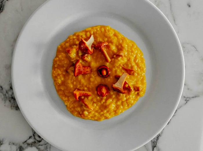 A dish of creamy golden rice garnished with mushroom slices.