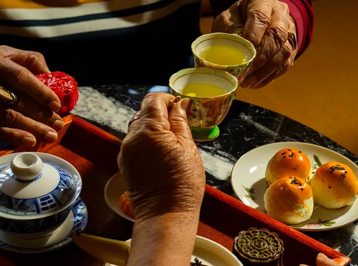 Cups of tea clink together, surrounded by a variety of sweets.