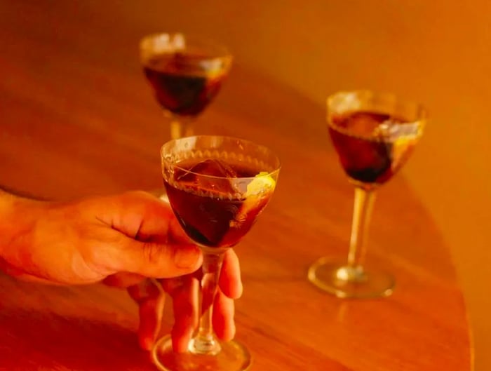 A hand grips a deep crimson cocktail, accompanied by two others close by.