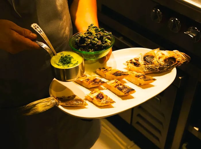 A server presents a platter featuring a whole fish sliced and adorned with various toppings.