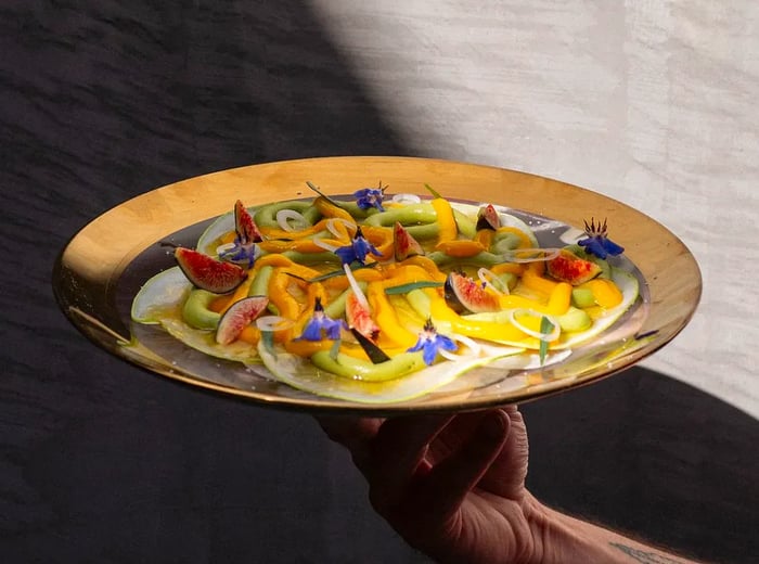 A waiter presents a platter filled with vibrant vegetables.