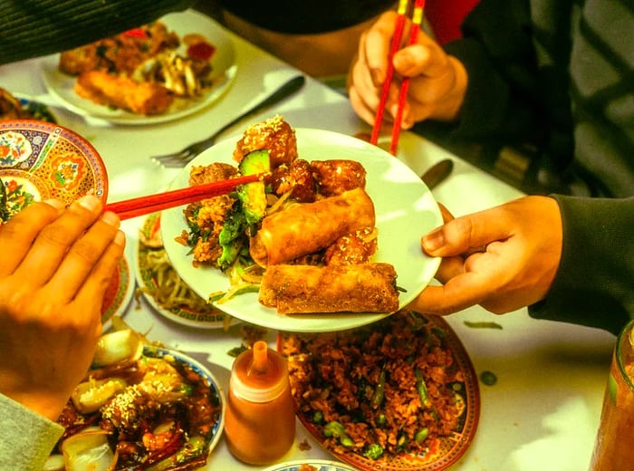 A diner selects a cucumber from a platter of spring rolls and assorted dishes.