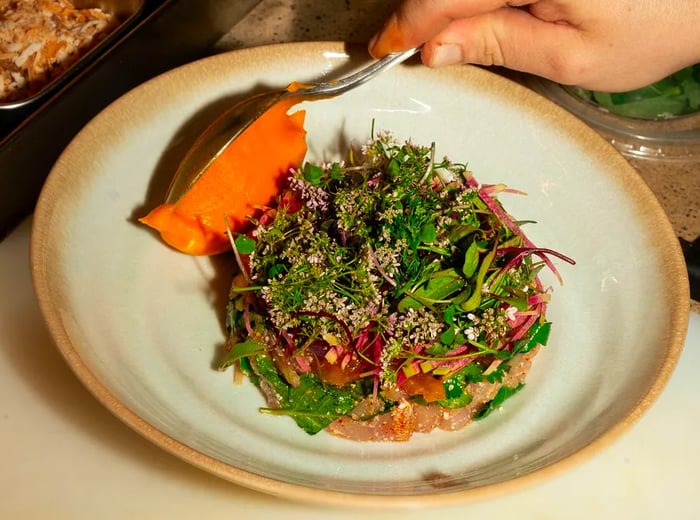 A chef finishes plating a vibrant larb, where the rice is adorned with flowers and fresh greens.