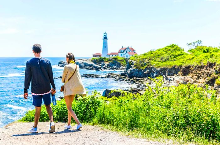 A young couple strolls along a trail beside the cliffs at Portland Head Light in Fort Williams Park, Cape Elizabeth, Maine, USA