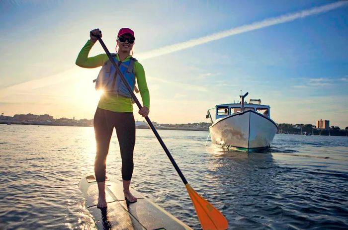 A cheerful young woman paddleboards across the harbor in Portland, Maine, USA