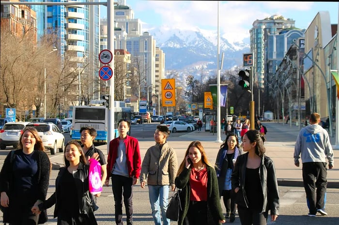 Local Kazakhs stroll through the streets surrounded by tall buildings, with snow-capped peaks visible in the distance, Almaty, Kazakhstan