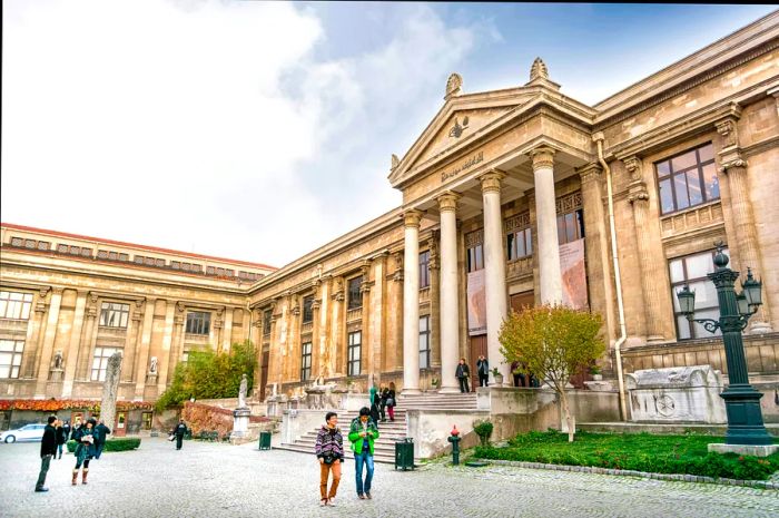 Pedestrians stroll outside the Istanbul Archaeology Museums on a cloudy day.