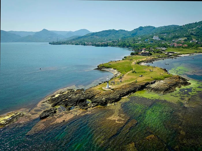 A narrow peninsula extends into the sea, capped by a white lighthouse at its tip.