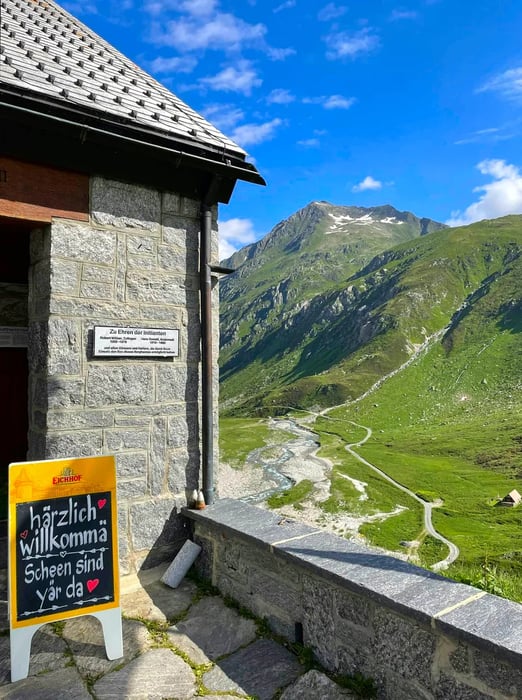 The entrance to a rustic mountain hut, with rolling hills and majestic mountains stretching into the distance.