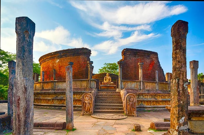 The remnants of a temple with crumbling brick walls and columns, featuring a Buddha figure at its center.