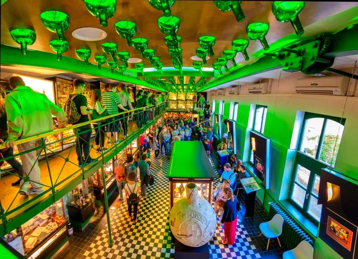 Visitors explore exhibits across two levels at the Zwack Unicum Factory museum, where green bottles are creatively incorporated into the ceiling design.