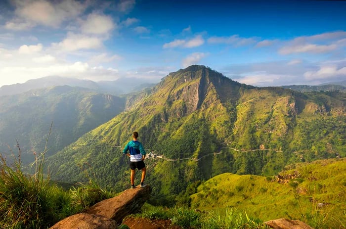 A person gazes from a peak towards another unique hill amidst a vibrant green landscape