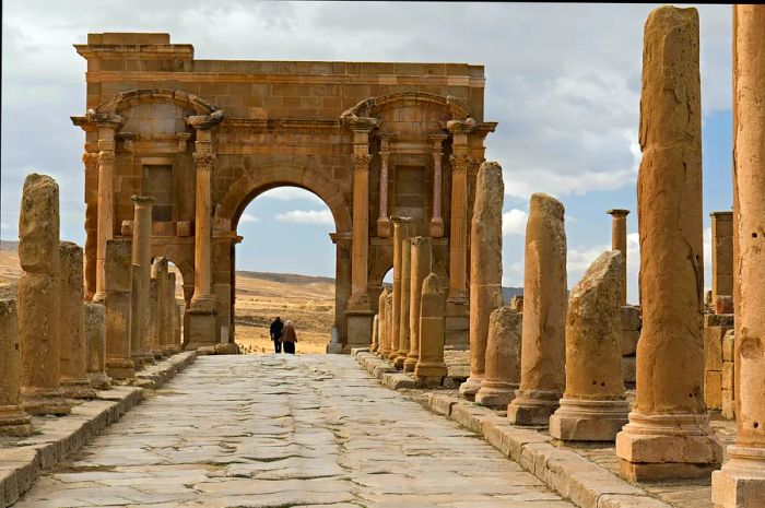 Visitors stroll past the Arch of Trajan amidst the ancient ruins of Timgad, Algeria