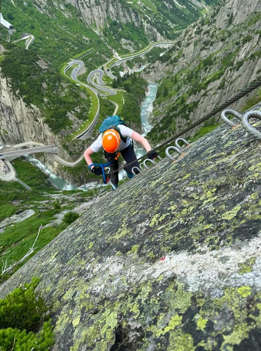 A climber scales a sheer cliff using cables and rungs secured to the rock face.