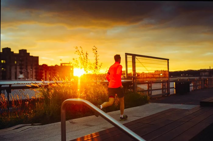 A runner clad in a bright orange jacket jogs along the New York High Line at sunset.