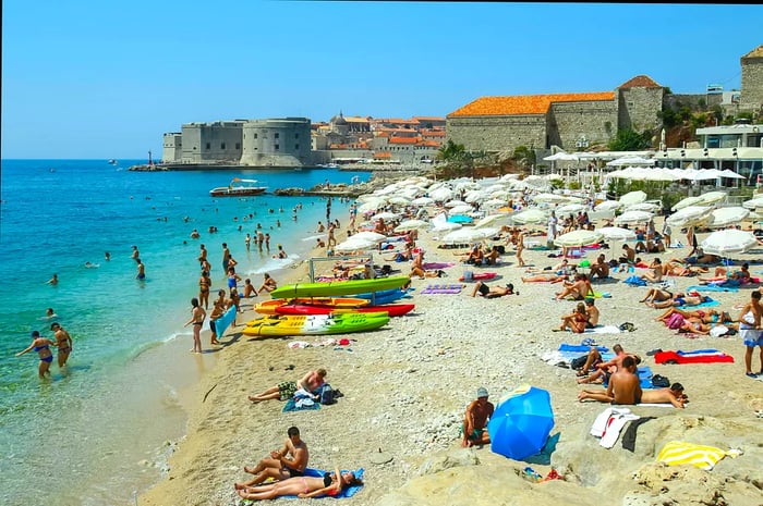 Visitors enjoying the sun and swimming at Banje beach, with Dubrovnik’s old town in the backdrop.