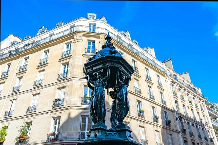 A picturesque green Wallace fountain in Paris, with a typical building in the background