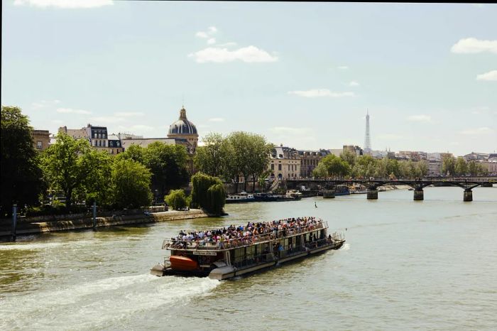 A view of a riverboat gliding along the Seine, with the Dome of the Institut de France and the Eiffel Tower in the background, Paris, France.