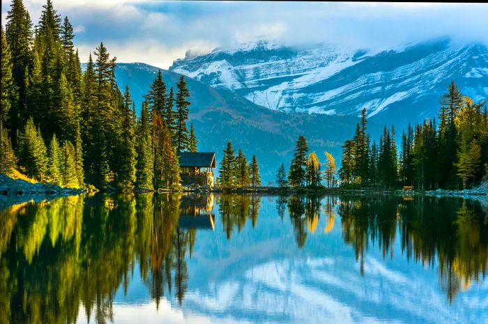 Mountains mirrored in a lake with a quaint wooden structure nestled in the cliffs