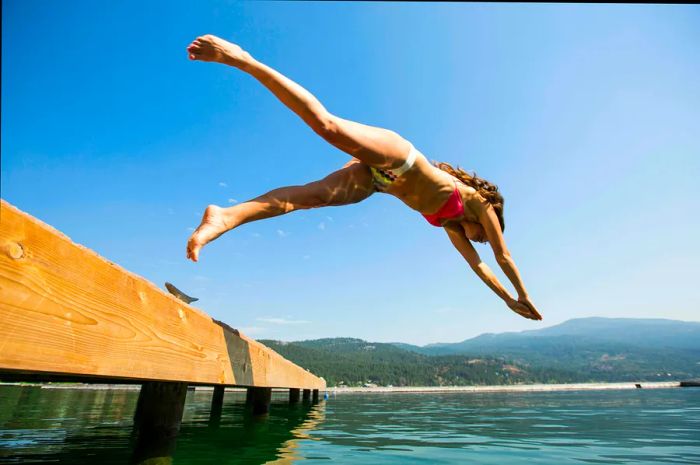 A woman leaps into the clear waters of Flathead Lake from a small dock.