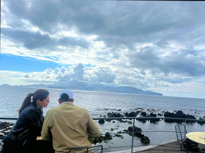 A couple enjoys the view from a table overlooking the sea.