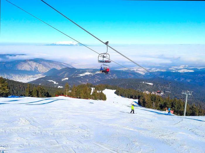 Skiers riding a chairlift with picturesque slopes in Bulgaria.