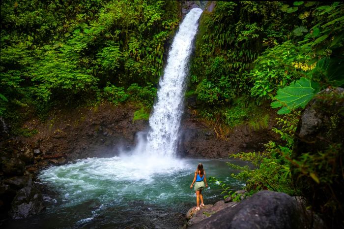 A solo woman stands by a waterfall in Costa Rica.