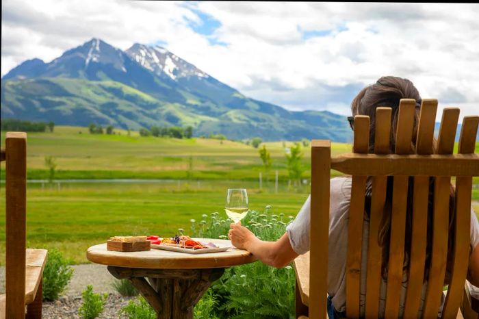 A woman enjoys a glass of wine while gazing at the stunning mountains of Montana