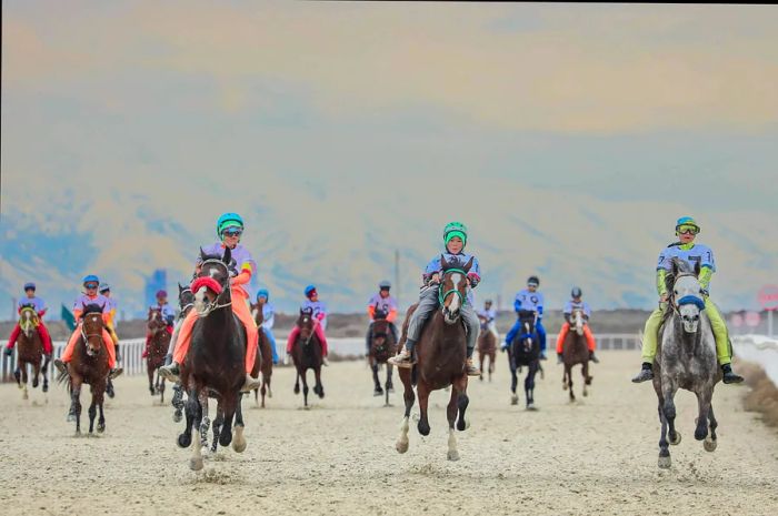 Horseback riders compete in a race on a sandy track.