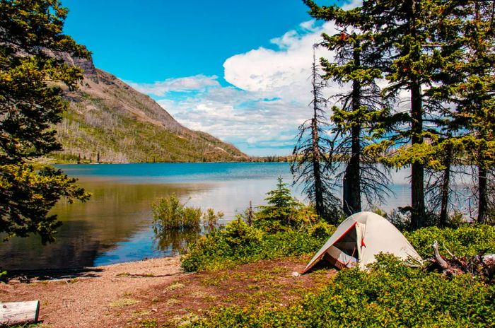 A tent set up beside a mountain lake under clear blue skies.