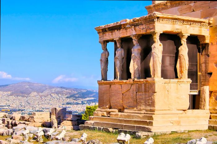 Enormous statues adorning the side of an ancient structure perched on a hill, overlooking a city.