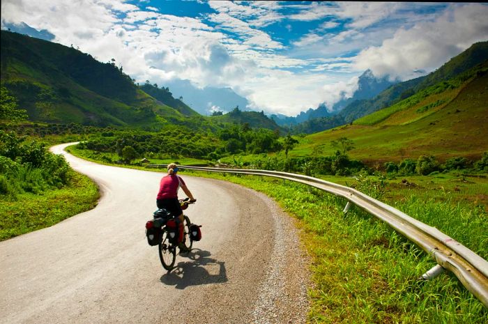 A cyclist pedals along a road in Laos.