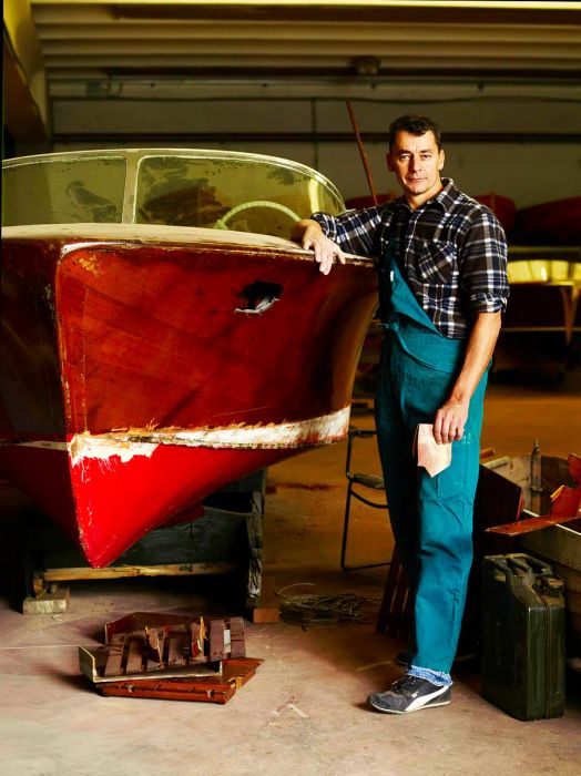 Image of a boat builder at his workshop by Lake Como, standing beside a traditional vessel.