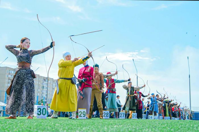 Women adorned in their nation's traditional attire participate in an archery competition, holding bows and arrows.