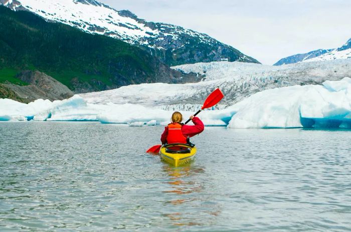 A woman kayaking solo beside a glacier in Alaska.