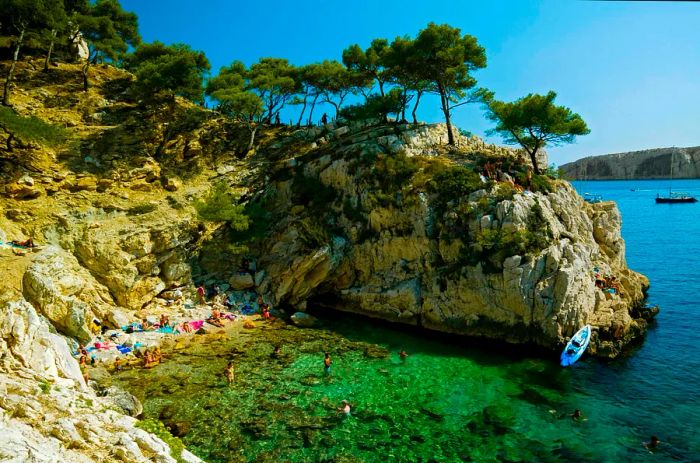 A picturesque cove nestled at the base of rugged sea cliffs, where visitors can be seen sunbathing and enjoying the water.