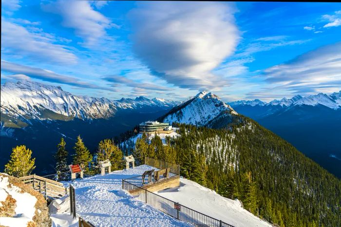 Snow blankets the wooden stairs and boardwalks, while the viewing platform offers a stunning overlook of Banff Gondola Station.