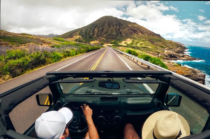 A couple drives a convertible along a scenic coastal road in Maui.