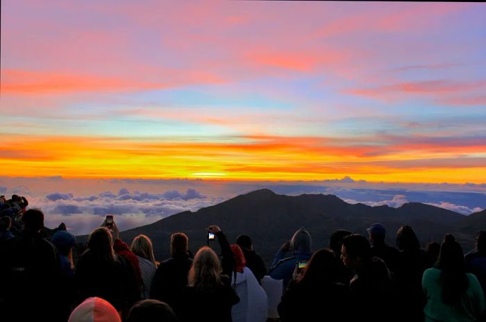 A group of individuals gathered at the Haleakalā summit at dawn, silhouetted by the rising sun.