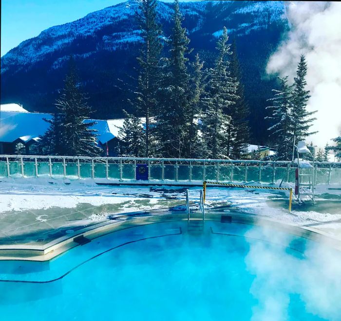 A steaming hot pool with a view of a snow-covered mountain range at Banff Upper Hot Springs