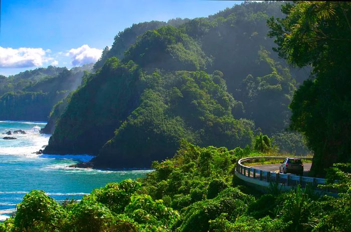 A car navigates a winding road along a cliffside adorned with lush greenery