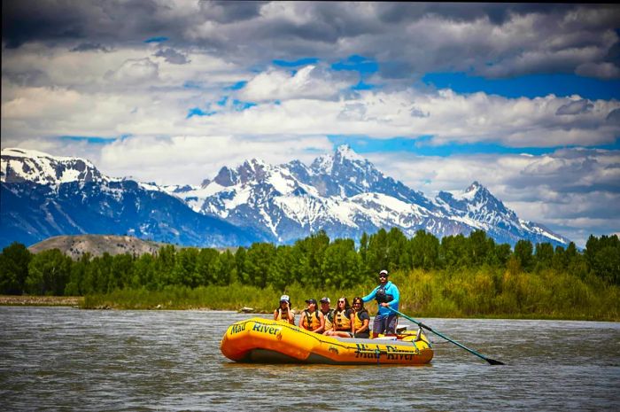 A group of paddlers navigating the Snake River with the majestic Grand Teton Mountains in the background.