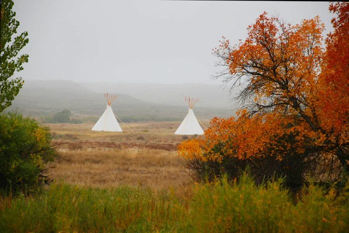 Tipis line the Laramie River at Fort Laramie National Historic Site, framed by stunning fall foliage and a backdrop of mist.