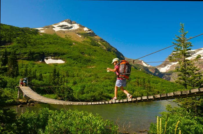 A young girl crosses a suspension bridge while hiking in Glacier National Park, Montana.