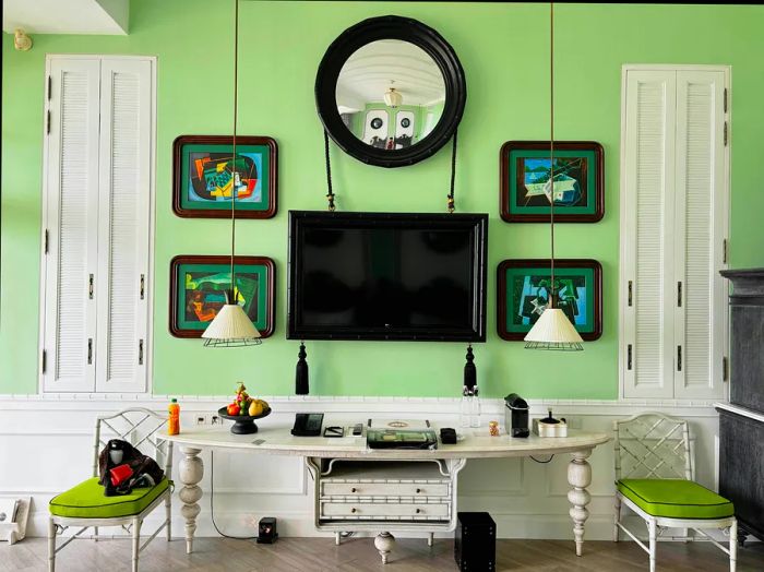 A television and artwork adorn a mint-colored wall above a sleek white table in a chic hotel room.