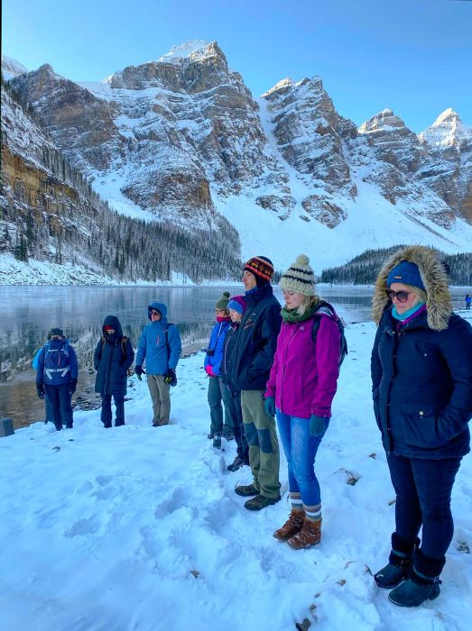 Individuals meditate on the shores of Moraine Lake, surrounded by deep snow during winter at Banff and Lake Louise