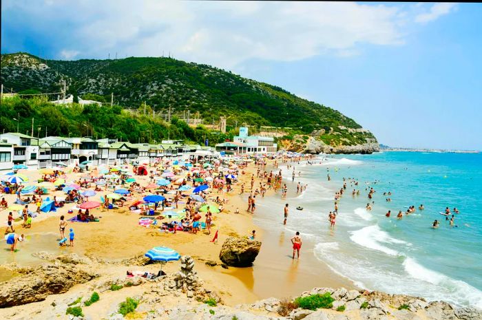 Visitors enjoying the sun, relaxing, and swimming at Garraf Beach, Sitges, Catalonia, Spain