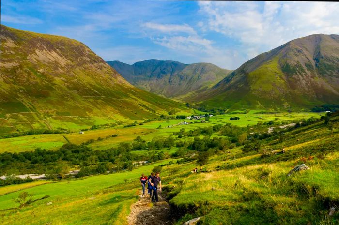 Hikers begin their ascent on a steep gravel path, with stunning green hills rolling in the background.