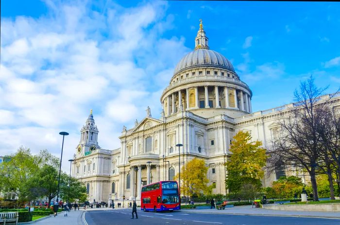 A red double-decker bus passes by a grand domed cathedral.