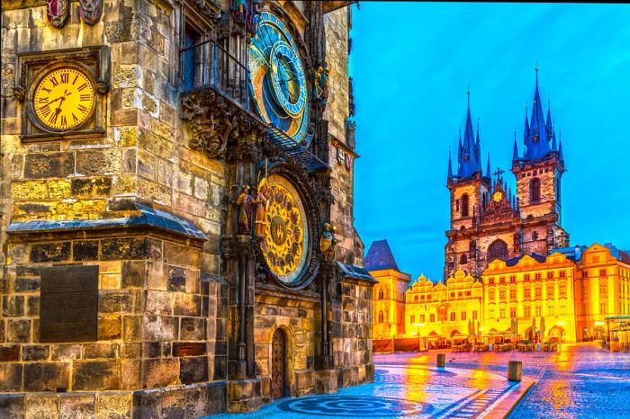 A misty city square in the evening featuring an ornate astronomical clock in gold and blue